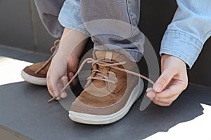 Little boy tying shoe laces on stairs outdoors, closeup photo