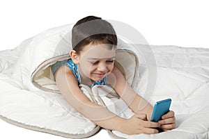 Little boy under blanket plays with smart phone