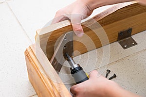 A little boy unscrews the wooden table with a screwdriver