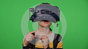 A little boy uses a virtual reality headset in a studio with a green background.