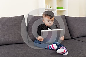 Little boy using digital tablet and sitting on sofa