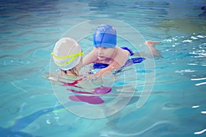 Little boy using the kickboard for learning to swim with trainer in the swimming pool