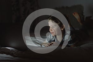 Little boy using laptop by night at home on the bedroom