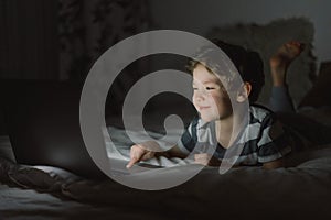 Little boy using laptop by night at home on the bedroom