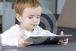 Little boy using touchscreen tablet at home. Happy smart child watching tutorials or playing game on tablet computer.