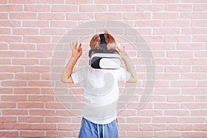 Little boy in virtual reality glasses in a white t-shirt on a brick wall background