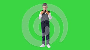 Little boy in waistcoat watching something on his phone and rounding his eyes in shock on a Green Screen, Chroma Key.