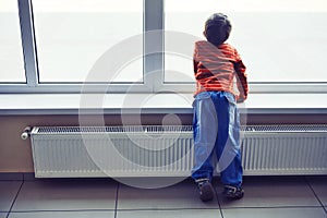 Little boy waiting at airport looking at window and enjoying planes arriving, rear view