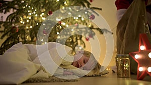 Little boy waiting Santa Claus under tree on Christmas Eve. Child is sleeping. Santa Claus brought gifts. Magic at Christmas and N