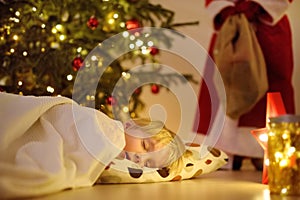 Little boy waiting Santa Claus under tree on Christmas Eve. Child is sleeping. Santa Claus brought gifts. Magic at Christmas and