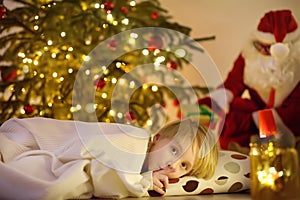 Little boy waiting Santa Claus under tree on Christmas Eve. Santa Claus brought gifts. Child not sleeping, but he does not show it