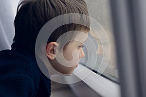 Little boy waiting by window for stop raining.