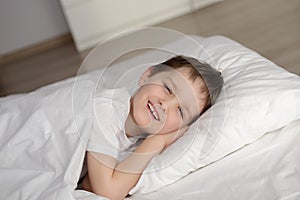 Little boy waking up in white bed with eyes open