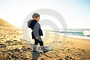 Little boy walking on beach at sunset, winter season