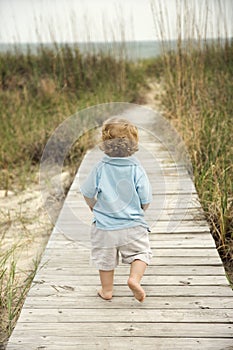 Little boy walking down beach walkway.