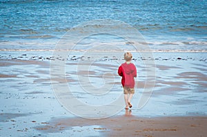 A little boy walking into the sea alone