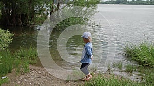 Little boy walks along the river. the child runs around the lake. slow motion. happy baby playing near the water.