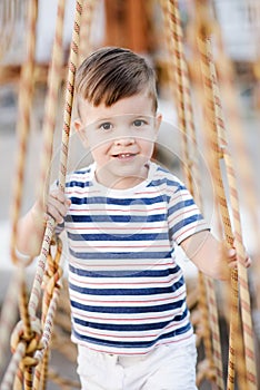 A little boy walks along a stretched wooden bridge in a rope town