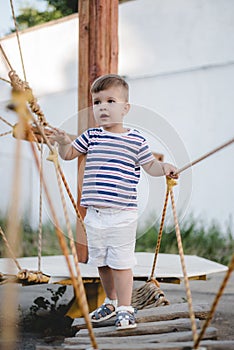 A little boy walks along a stretched wooden bridge in a rope town