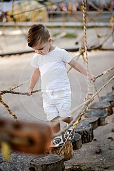 A little boy walks along a stretched wooden bridge in a rope town