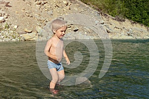 A little boy walks on the water of a mountain river. Rocks in the background