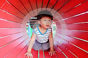 The little boy was in the wooden tunnel in the playground