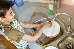 Little boy washing the dishes in the kitchen sink