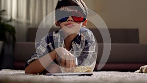 Little boy watching movies in 3d glasses and eating popcorn, enjoying at home