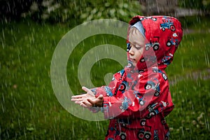 Little boy in a waterproof jacket in tractors catch the rain. Child having fun outdoors in summer shower