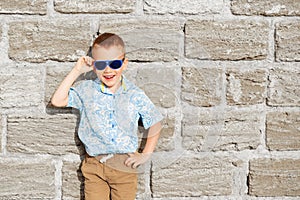 little boy wearing blue mirror sunglasses against the yellow brick wall outdoors