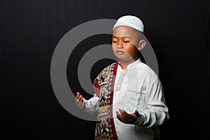 A little boy wearing a cap is praying isolated on black background