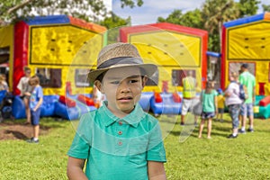 A little boy wearing a fedora hat is getting upset by the inflatable bounce house