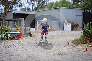 Little boy wearing gum boots jumping and splashing in puddle