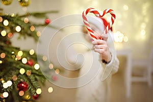 Little boy wearing Santa hat ready for celebrate Christmas. Cute child decorating Christmas tree with big sweet candy. Baby hold