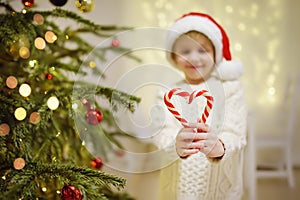 Little boy wearing Santa hat ready for celebrate Christmas. Cute child decorating Christmas tree with big sweet candy. Baby hold