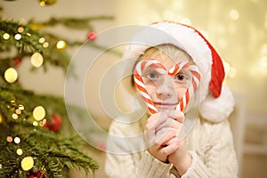 Little boy wearing Santa hat ready for celebrate Christmas. Cute child decorating Christmas tree with big sweet candy. Baby looks