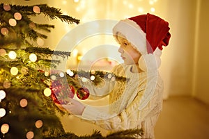 Little boy wearing Santa hat ready for celebrate Christmas. Cute child decorating the Christmas tree with glass toy. Baby hopes of