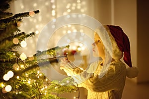 Little boy wearing Santa hat ready for celebrate Christmas. Cute child decorating the Christmas tree with glass toy. Baby hopes of