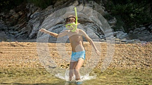 Little boy wearing snorkeling mask and breathing tube running from the beach in sea and diving underwater