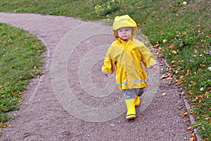 Little boy wearing yellow rain coat walking in the park