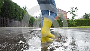 Little boy wearing yellow rubber boots jumping in puddle of water on rainy summer day in small town. Child having fun.