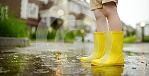 Little boy wearing yellow rubber boots walking on rainy summer day in small town. Child having fun. Games for children in rain