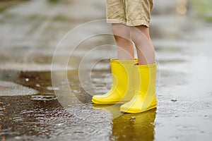 Little boy wearing yellow rubber boots walking on rainy summer day in small town. Child having fun. Outdoors games for children in