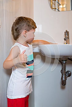 Little boy wets his hands in the washbasin