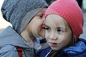 Little boy whispers a secret to girl wearing winter hats