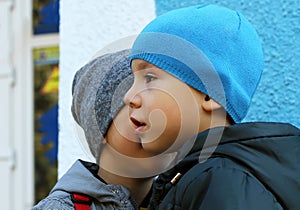 Little boy whispers a secret to his friend wearing winter hats