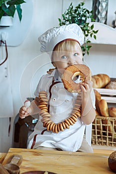 little boy in white chef uniform holding a loaf and candy in the bakery, bread shop