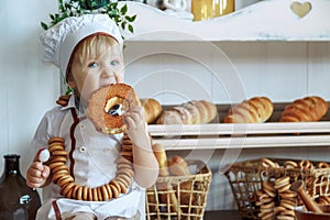 little boy in white chef uniform holding a loaf and candy in the bakery, bread shop