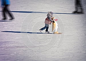 Little boy in winter clothes skating on ice rink