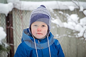 A little boy in a winter hat and jacket while walking on a cold winter snowy day